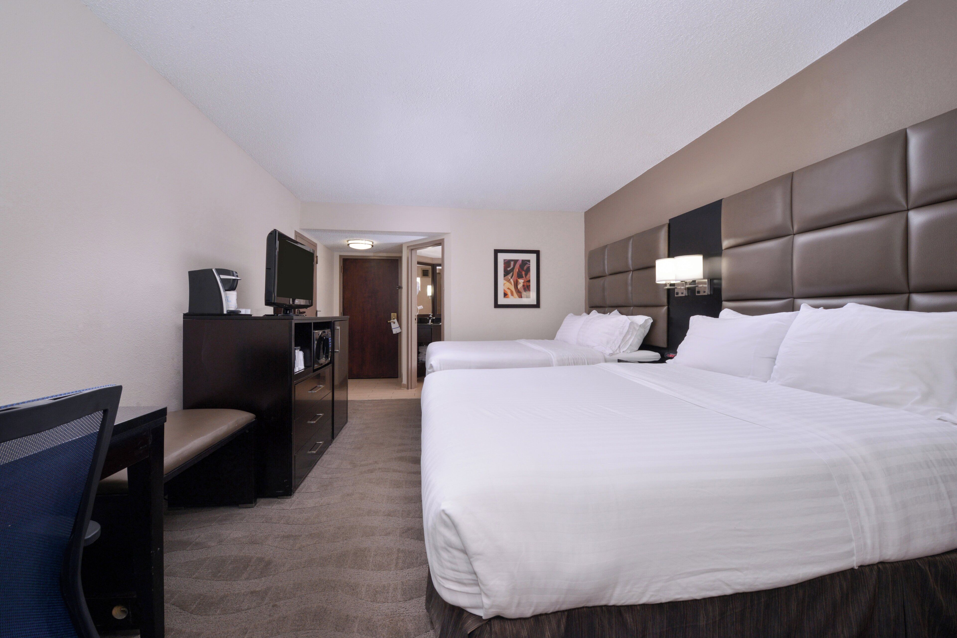 A hotel room with two beds, a desk with a chair, a television, and a door leading to a bathroom.