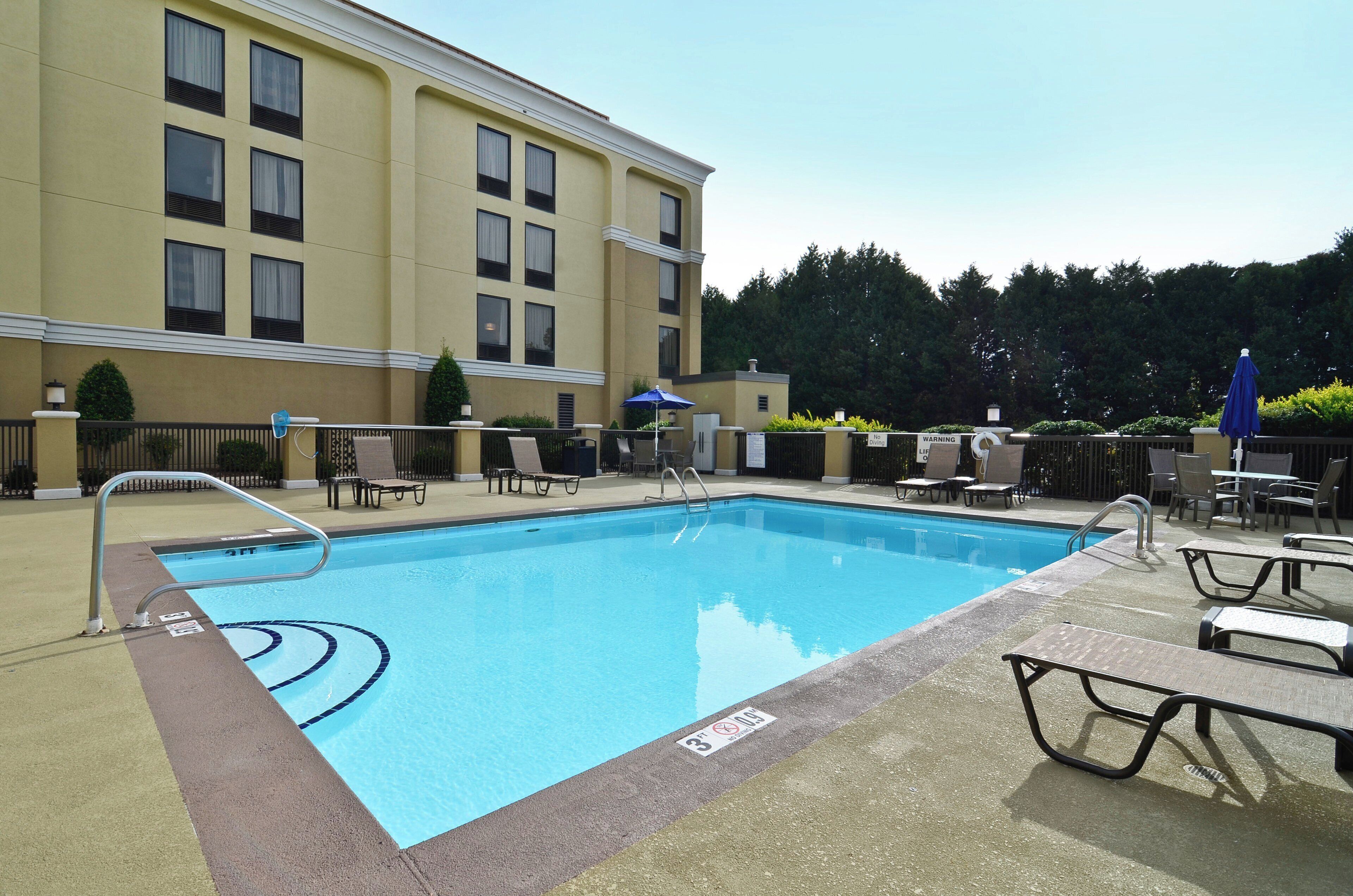 A rectangular swimming pool with a metal ladder on one side, surrounded by lounge chairs and umbrellas.