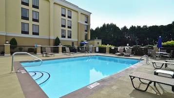 A rectangular swimming pool with a metal ladder on one side, surrounded by lounge chairs and umbrellas.
