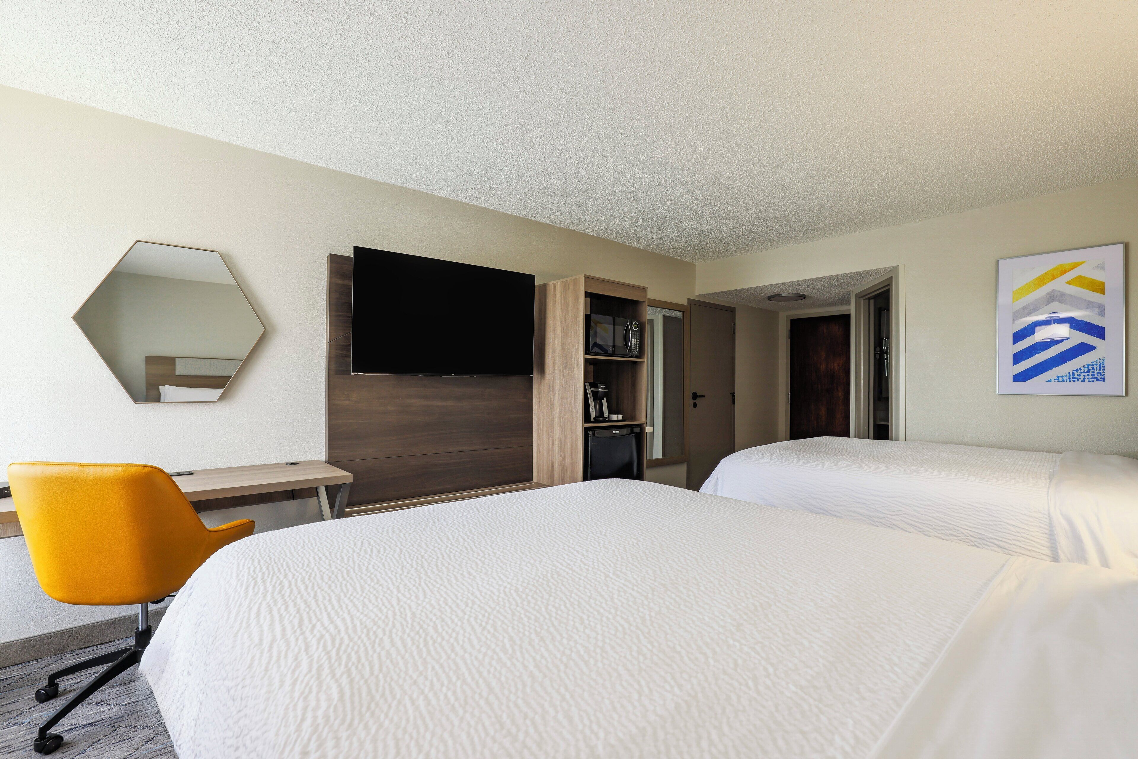 A hotel room with two beds, a desk, a chair, a television, and a door leading to another room.