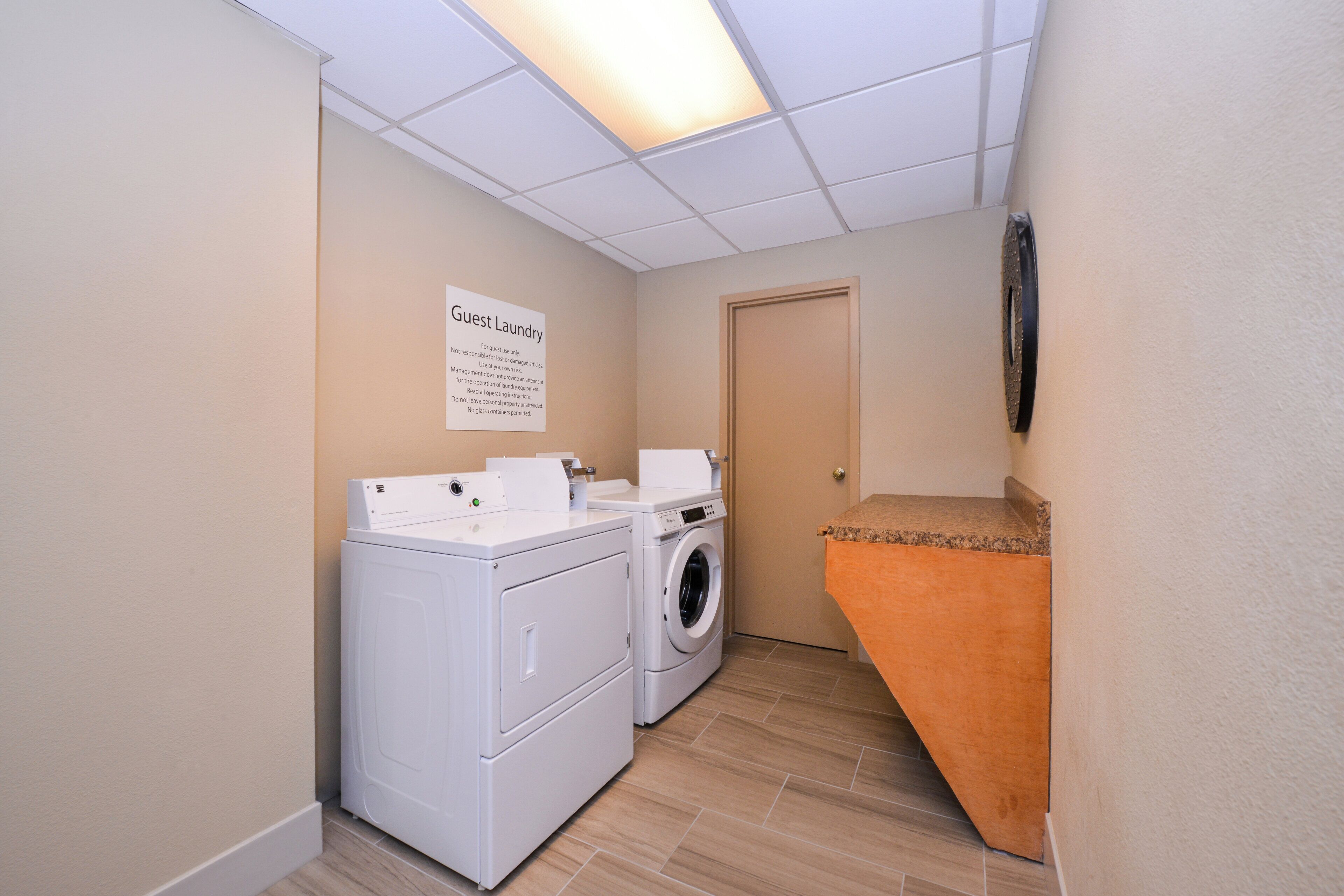 A laundry room with a sign indicating it's for guest use, a washing machine, a dryer, and a small orange step leading to a door.