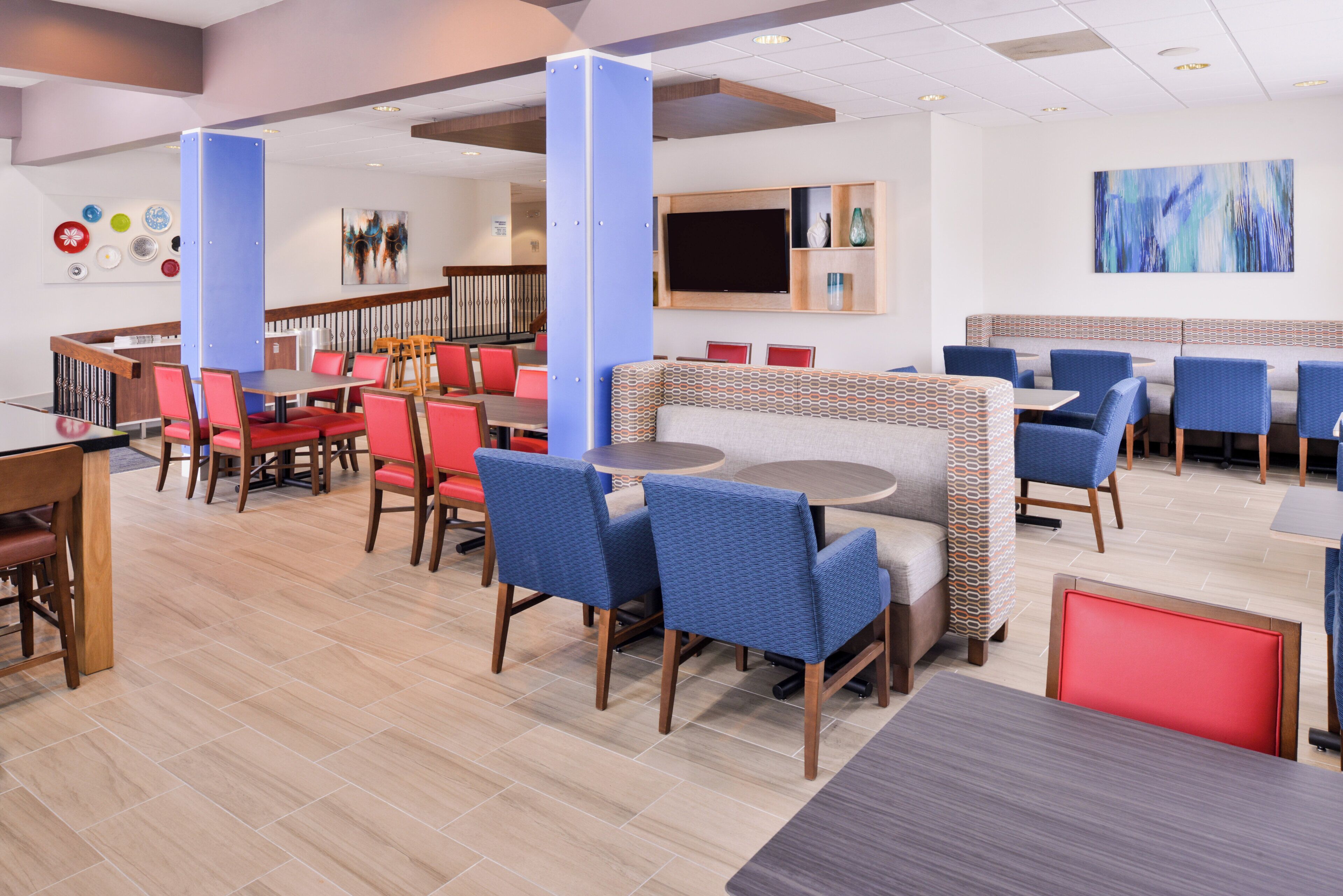 A modern restaurant interior with multiple dining areas, including booths and tables, and a staircase leading to an upper level.