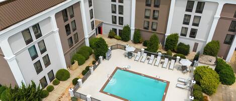 A rooftop pool area with a rectangular pool, surrounded by lounge chairs and umbrellas, and bordered by a low fence.