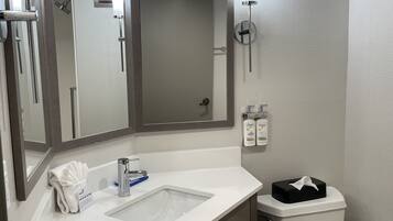 A bathroom with a white sink, a mirror, a towel rack, a toilet, and a shower.