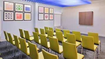 Un salón de conferencias con hileras de sillas amarillas, una pizarra y obras de arte geométricas enmarcadas en las paredes.