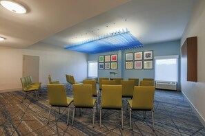 A conference room with yellow chairs arranged in a semi-circle, a patterned carpet, and a ceiling with a blue light fixture.