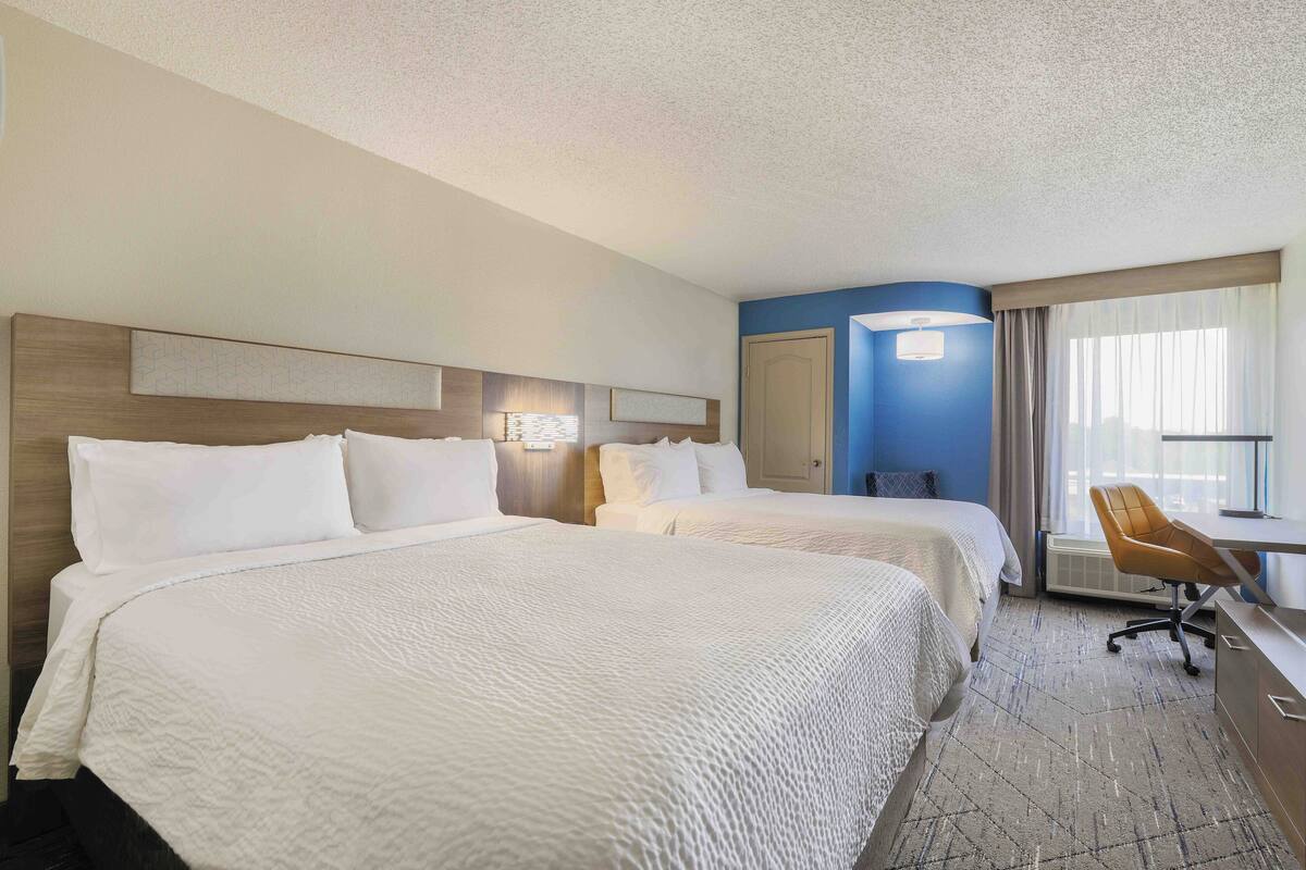 A hotel room with two beds, a desk, and a chair.