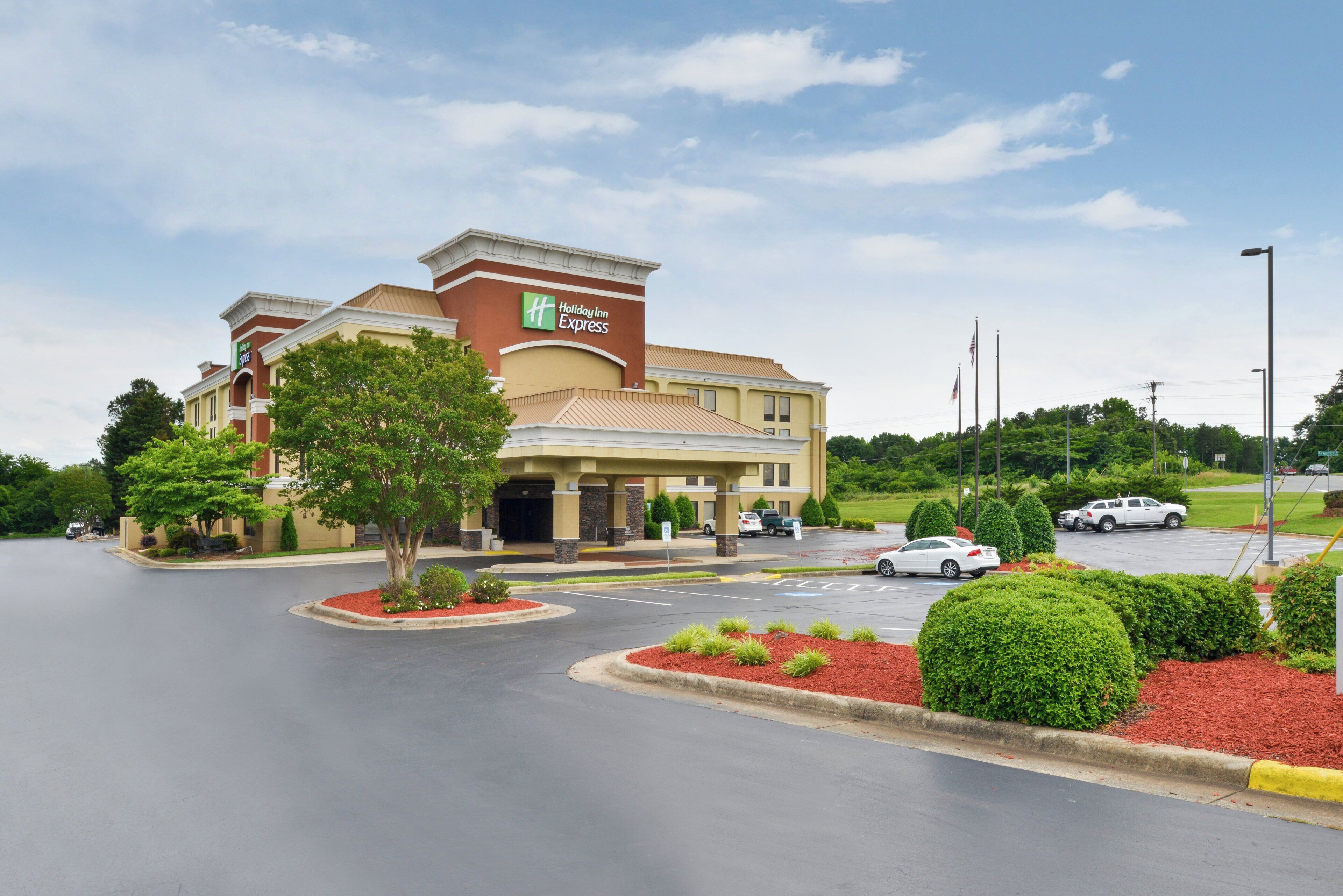 Un hôtel Holiday Inn Express doté d’un parking et d’un espace paysager agrémenté de paillis rouge et d’arbustes verts.
