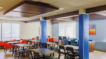 A modern dining area with multiple tables and chairs, a reception desk, and large windows allowing natural light.