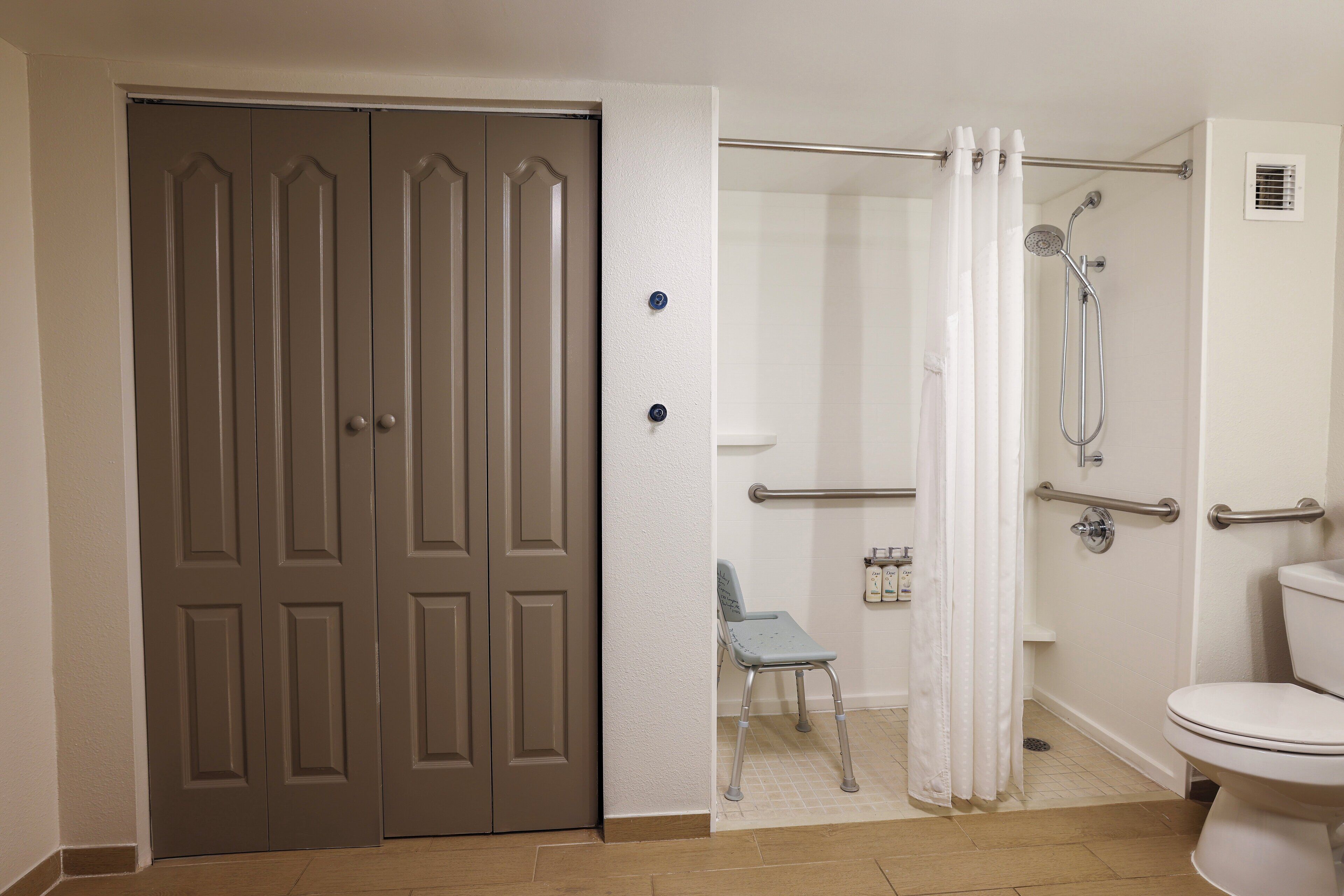 A bathroom with a toilet, shower, and a chair.