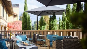 An outdoor patio area with wicker furniture, a fire pit, and a large umbrella providing shade. - Hotel Abrego (Monterey)