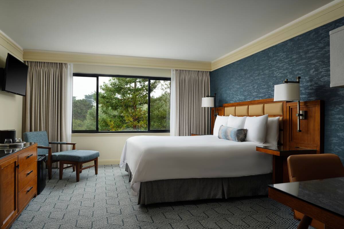 A hotel room with a large bed, a desk, a chair, a TV, and a window with curtains.
