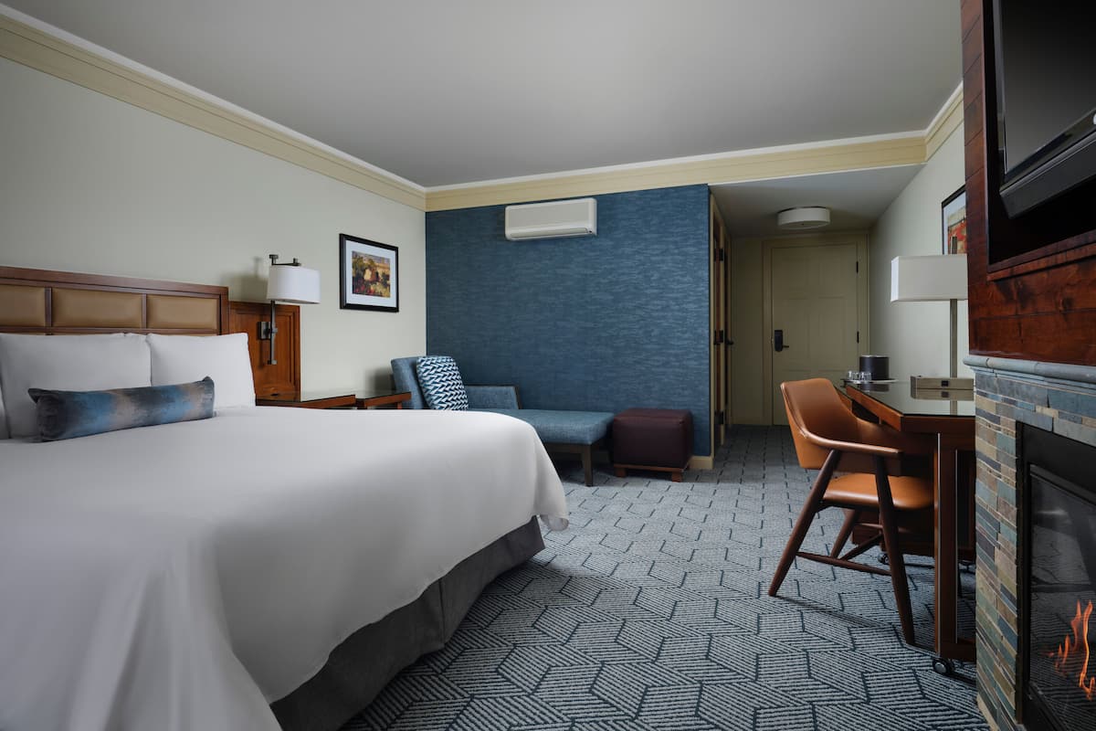 A hotel room with a large bed, a desk, a chair, a fireplace, and a blue accent wall.