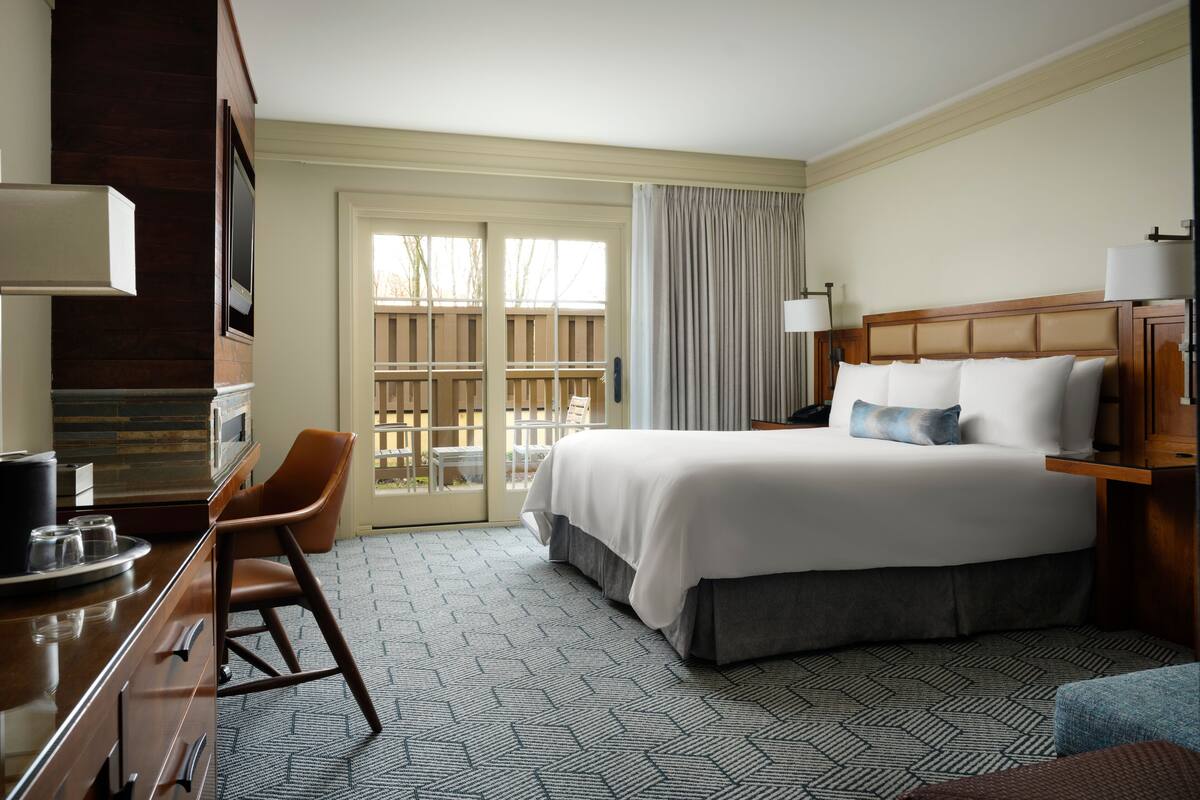 A hotel room with a bed, a desk, a chair, a TV, and a view of the outdoors.