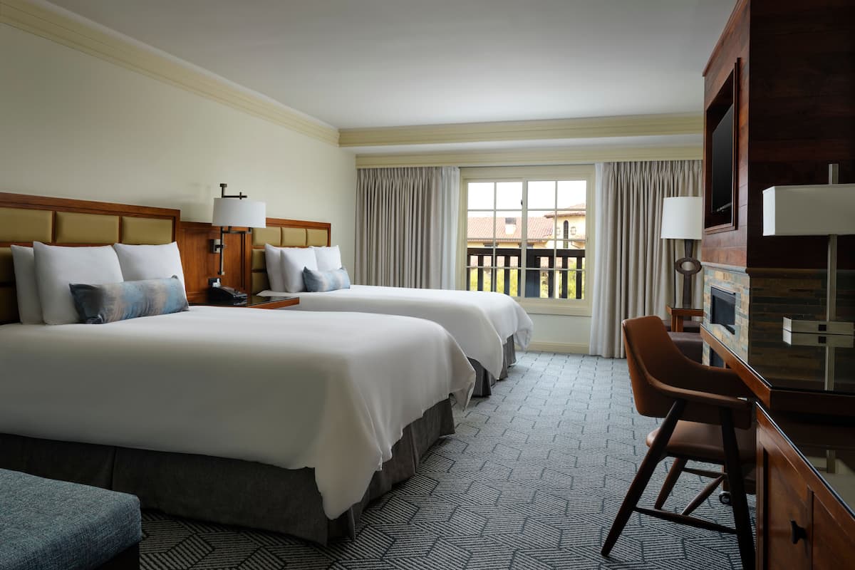 A hotel room with two beds, a desk, a chair, a TV, and a window with curtains.
