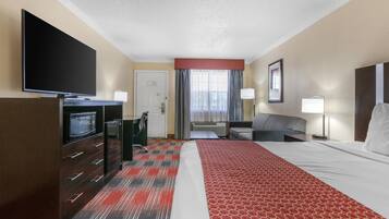 Habitación de hotel con cama, televisor, escritorio con microondas, silla, sofá y ventana con cortinas.