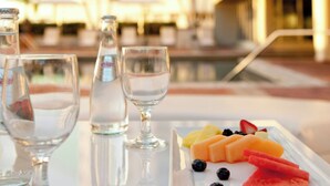 A table with a fruit platter and glasses, overlooking a pool and a hotel building. - Marriott Miami Dadeland (Miami)