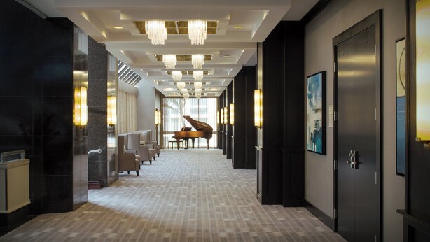 A hotel corridor with chandeliers, a grand piano, seating area, and artwork on the walls. - Marriott Miami Dadeland (Miami)