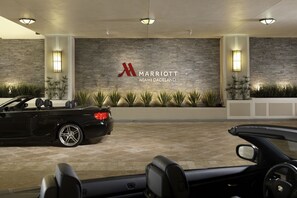 Un coche descapotable negro estacionado frente al hotel Marriott Miami Dadeland, con fachada de piedra y señalización iluminada.