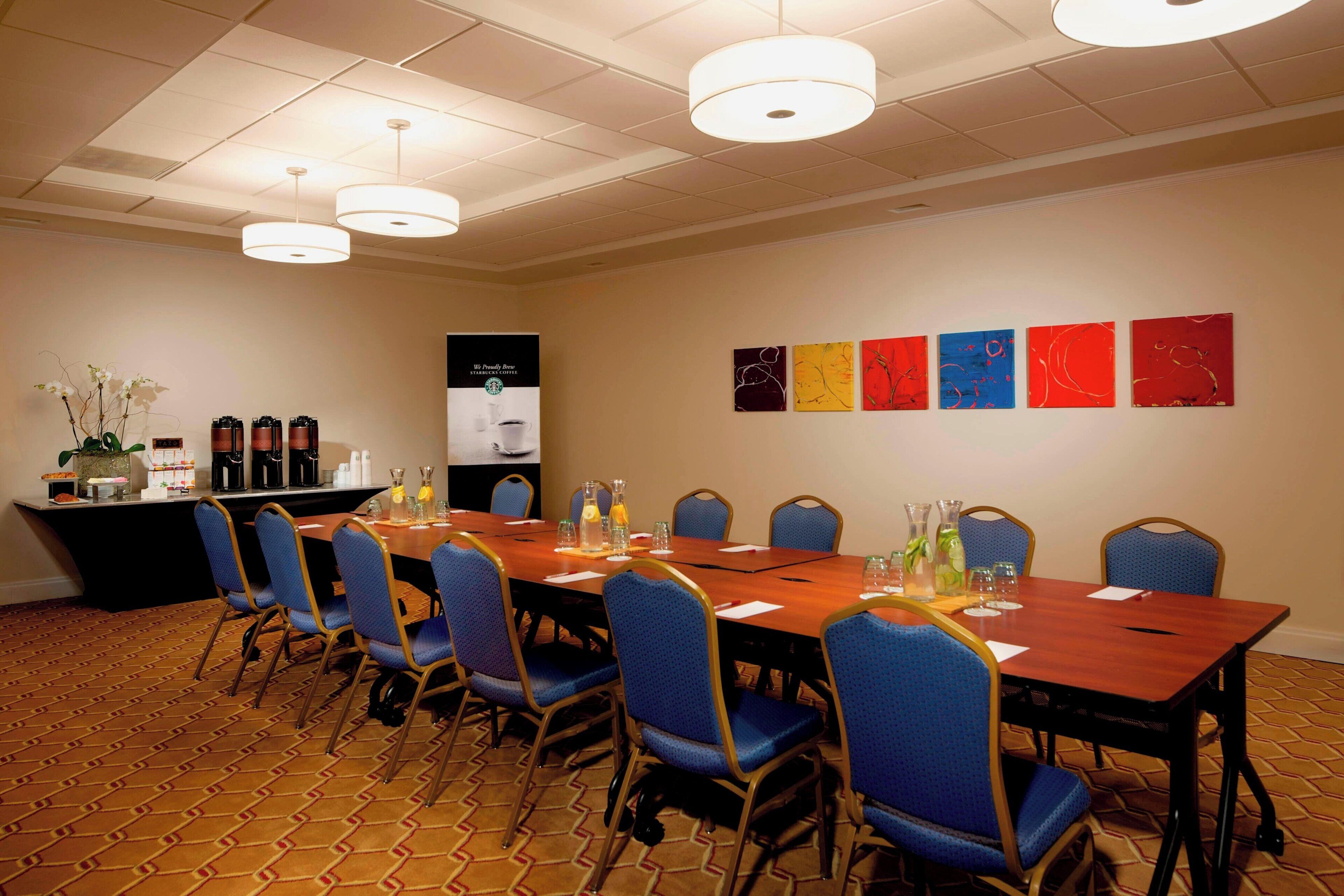 A conference room with a long table, blue chairs, and a coffee station.
