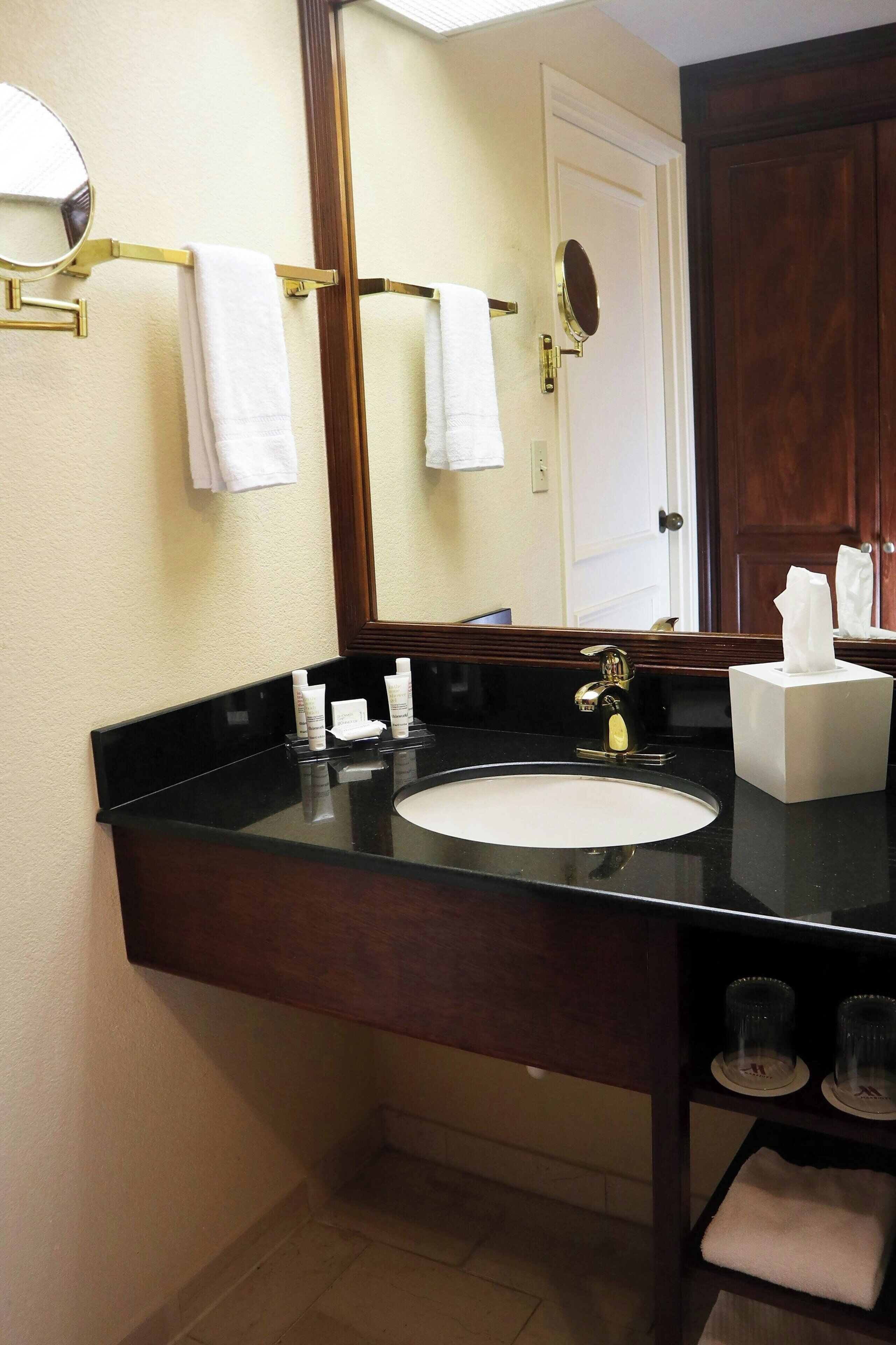 Une salle de bain avec un comptoir noir, un lavabo blanc, un miroir et un porte-serviettes.