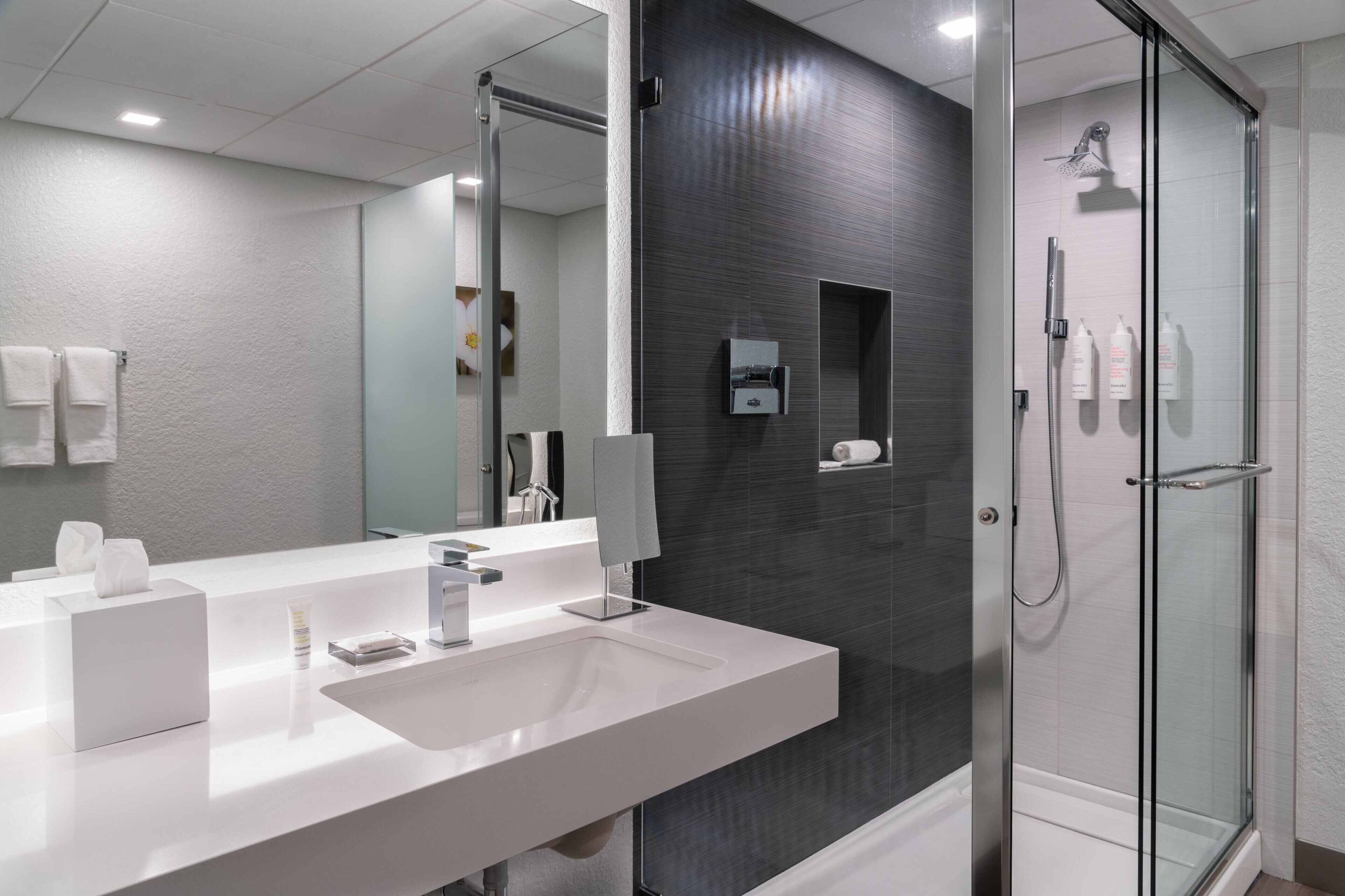 A modern bathroom with a white sink, mirror, and glass shower enclosure.