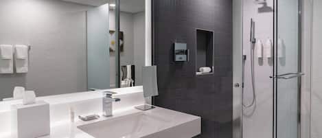 A modern bathroom with a white sink, mirror, and glass shower enclosure.