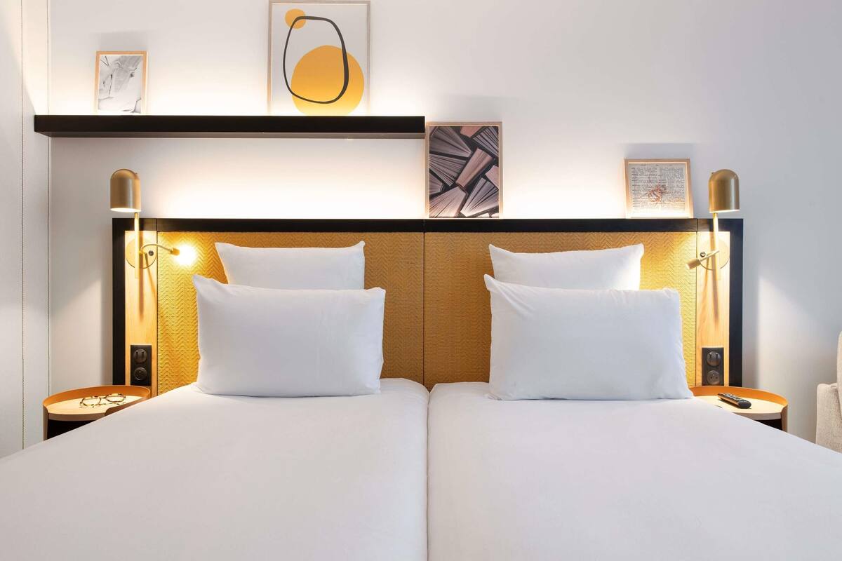 A double bed with white linens, two bedside tables with lamps, and artwork on the wall.