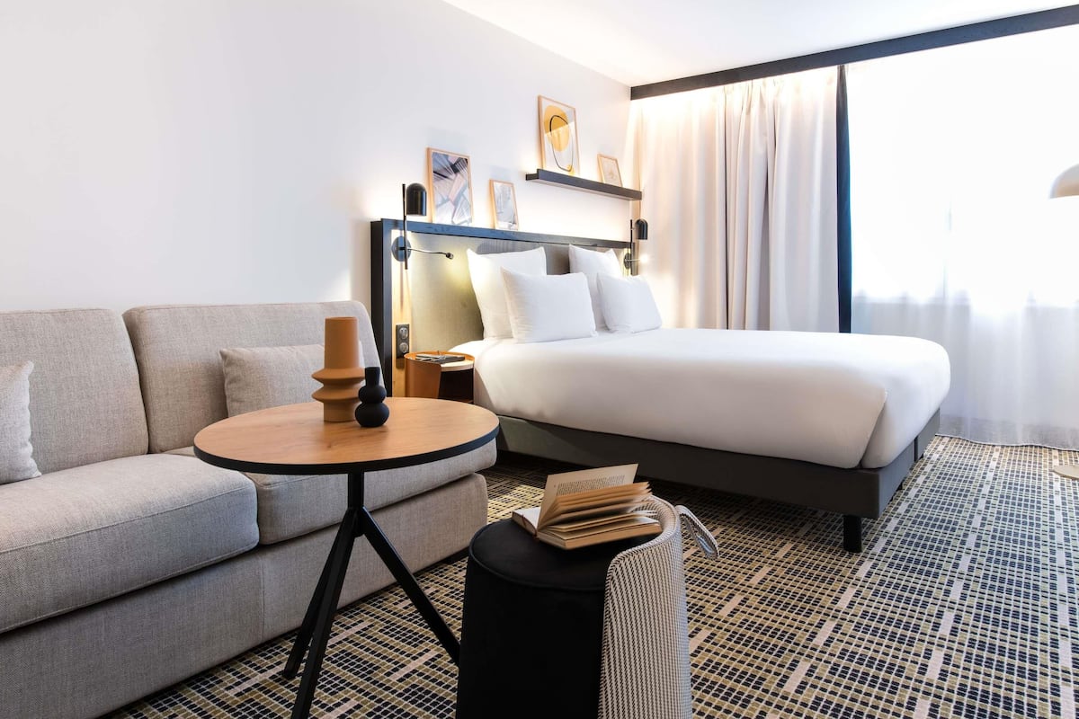 A hotel room with a bed, a sofa, a small table with a candle, and a bookshelf.