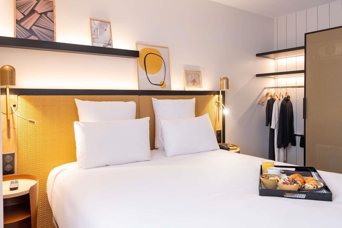 A hotel room with a large bed, bedside tables, a wardrobe, and artwork on the walls.