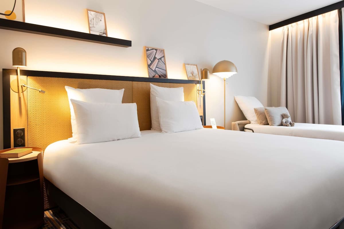 A hotel room with a large bed, bedside tables, a chair, and a window with curtains.
