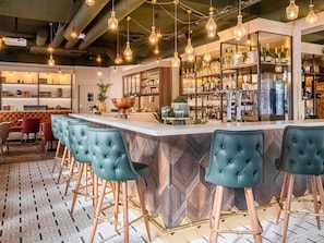 A bar area with a herringbone-patterned bar counter, tufted bar stools, hanging pendant lights, and a wine display. - Mercure Paris Bercy Bibliothèque (Paris)