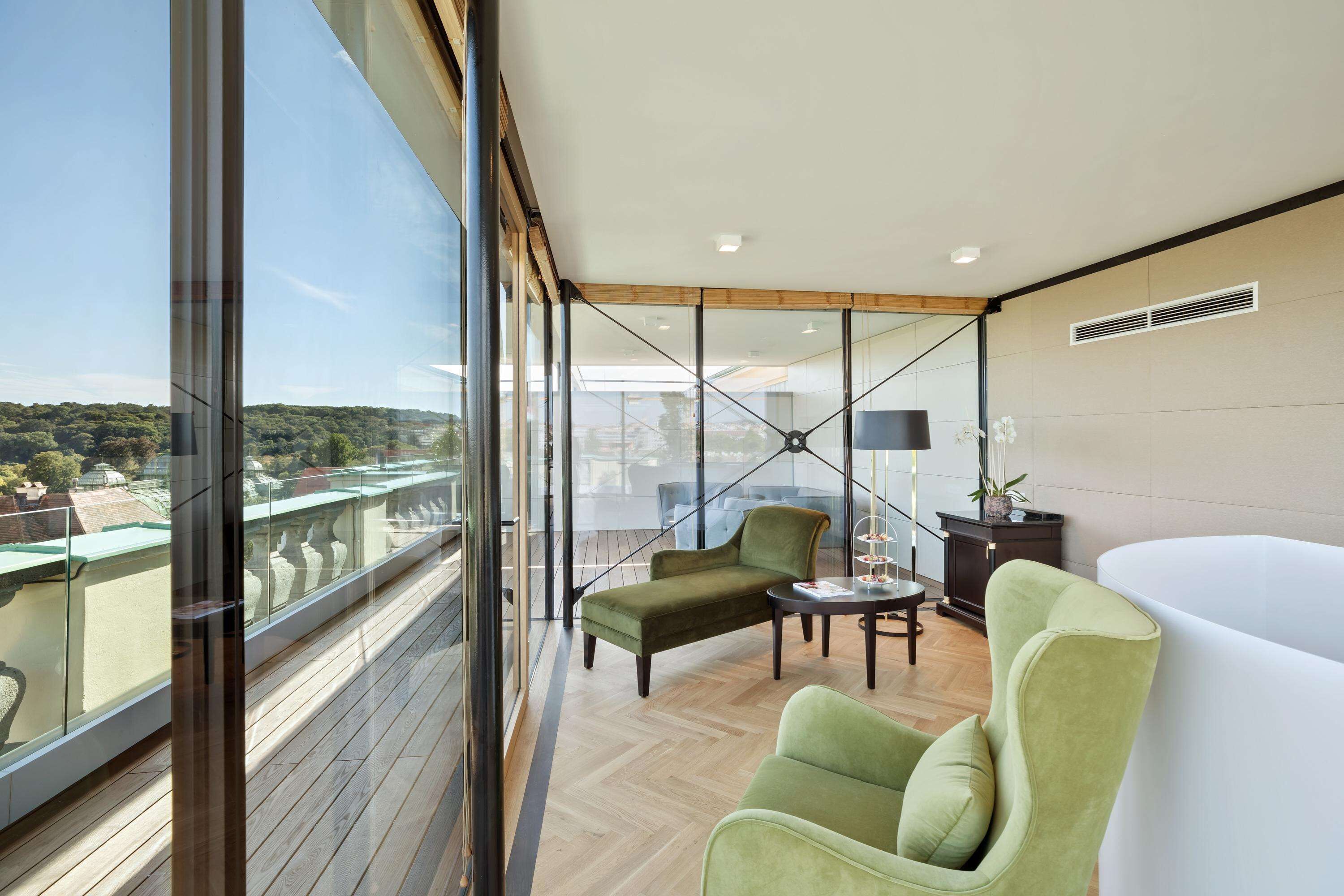 Un balcón moderno con vistas a un paisaje urbano, amoblado con un sillón verde, una mesita y un sofá blanco.