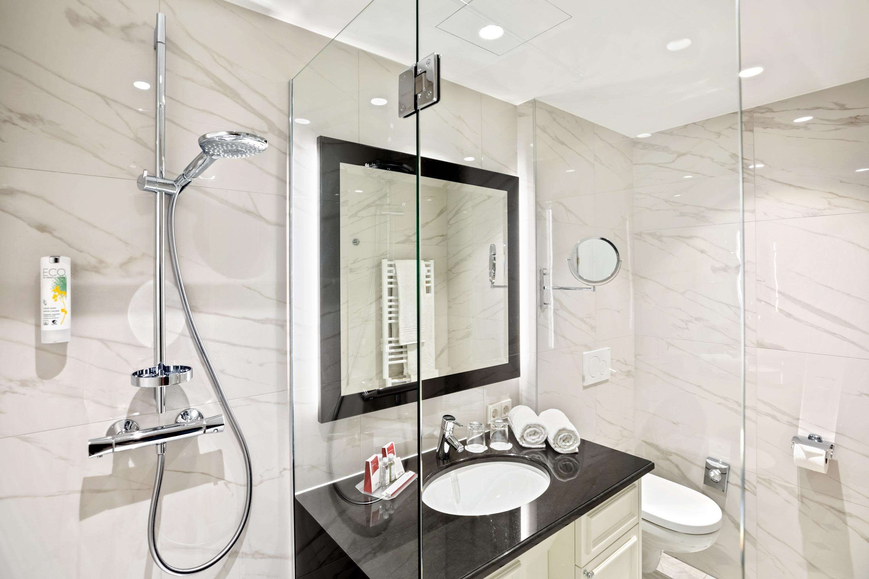 A modern bathroom with a glass-enclosed shower, a large mirror, a sink, and a toilet.