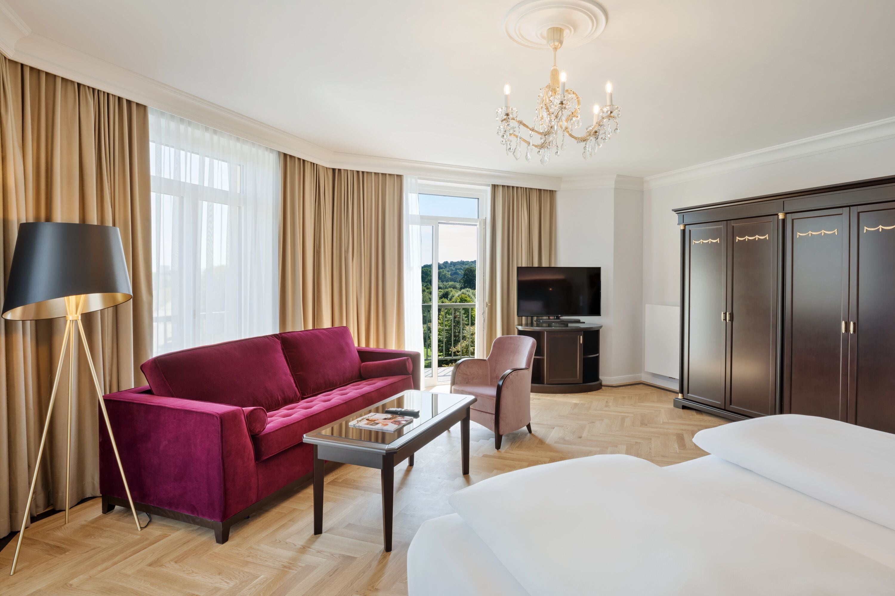 Una habitación de hotel moderna con una cama grande, un sofá rojo, una mesita de centro, un televisor y un armario.