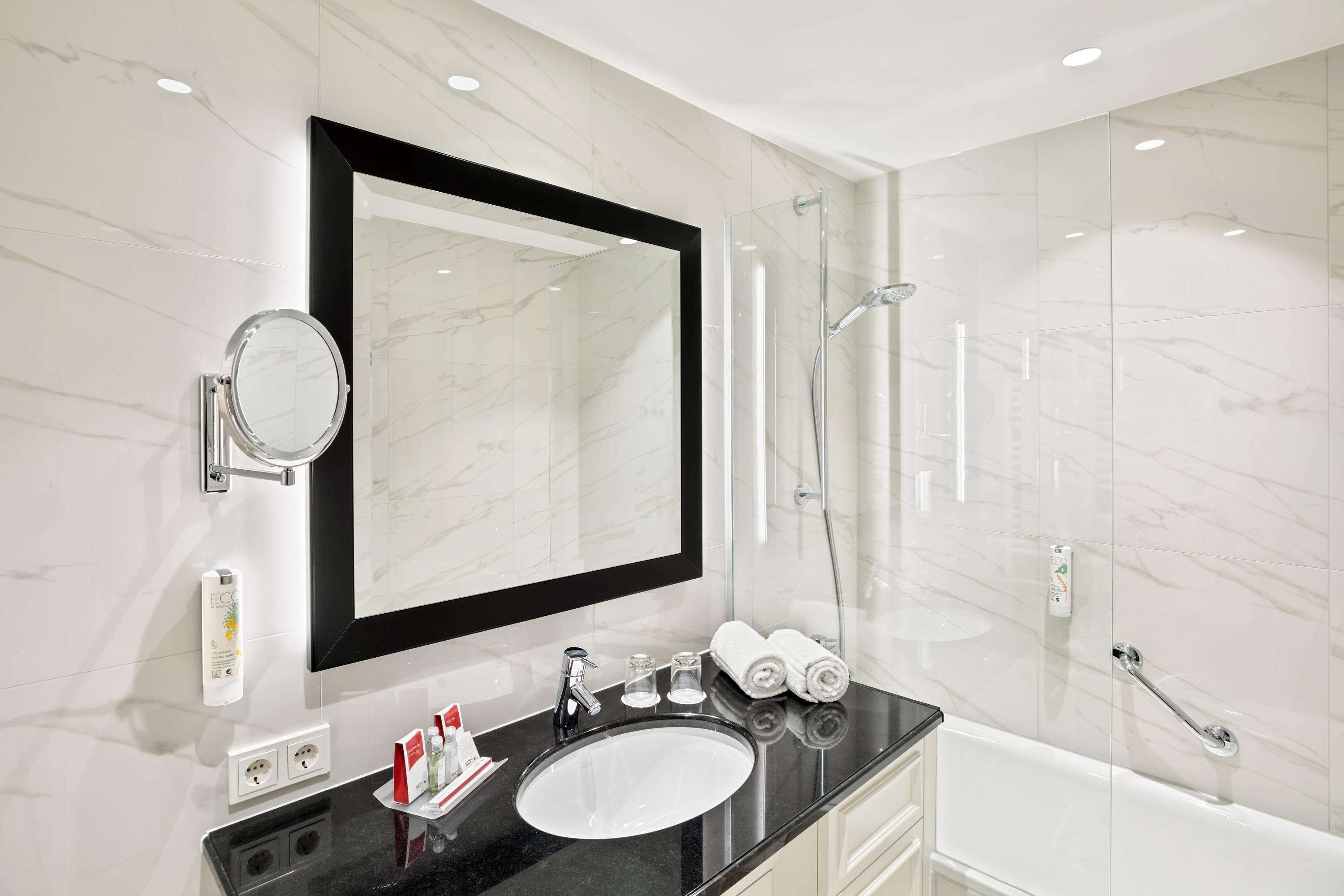 Une salle de bain moderne avec un grand miroir, un meuble-lavabo rond, une baignoire et une douche à l’italienne.