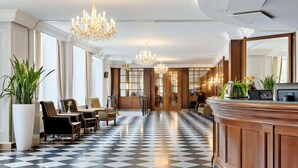 Un vestíbulo de hotel con piso a cuadros, una recepción y varias áreas de descanso con sillas.