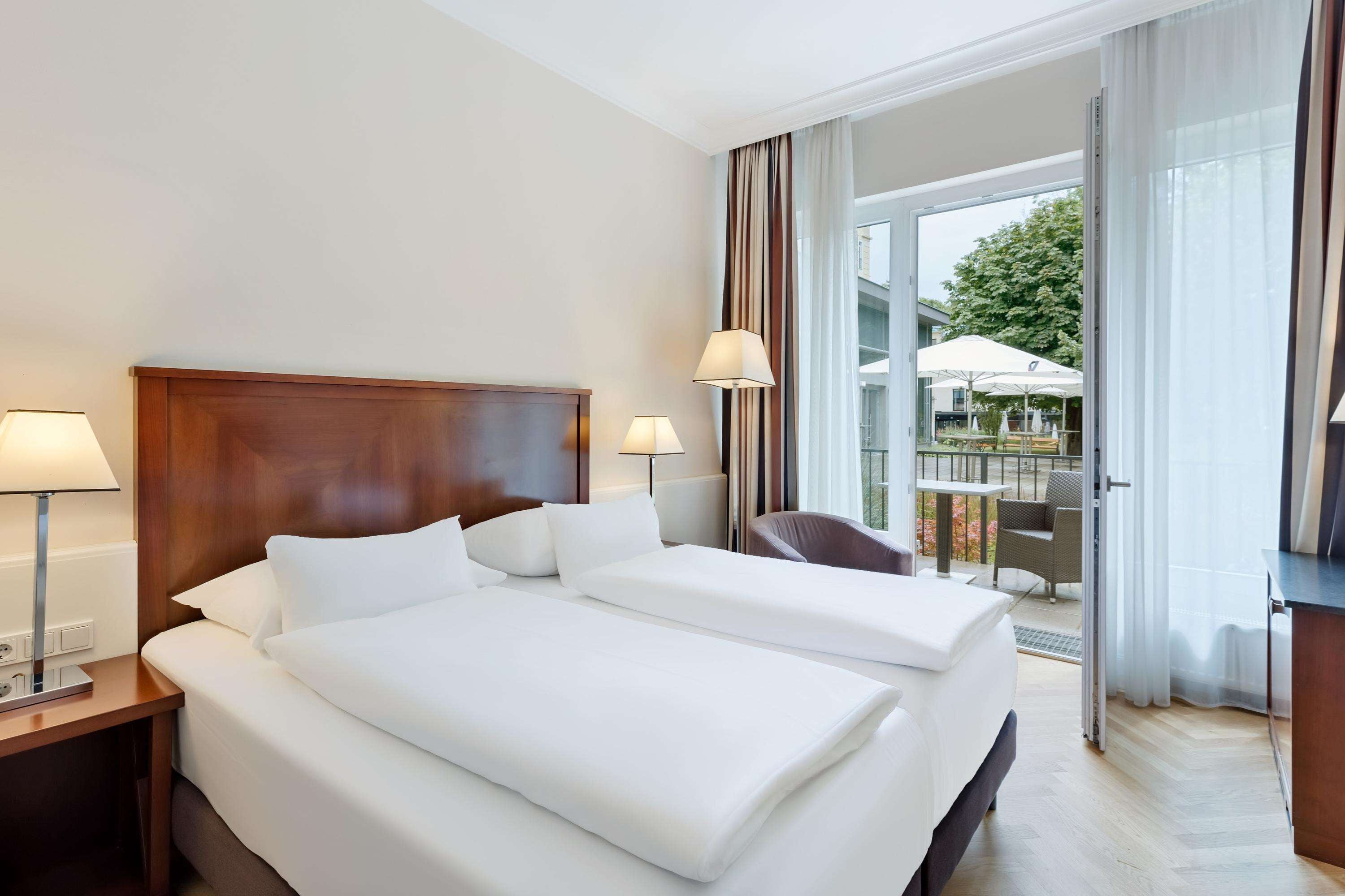 Habitación de hotel con dos camas, cabecera de madera y vista a un área de estar exterior a través de un ventanal.