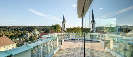 Un edificio moderno con balcón de cristal que da a un paisaje urbano, incluyendo una iglesia con dos torres.