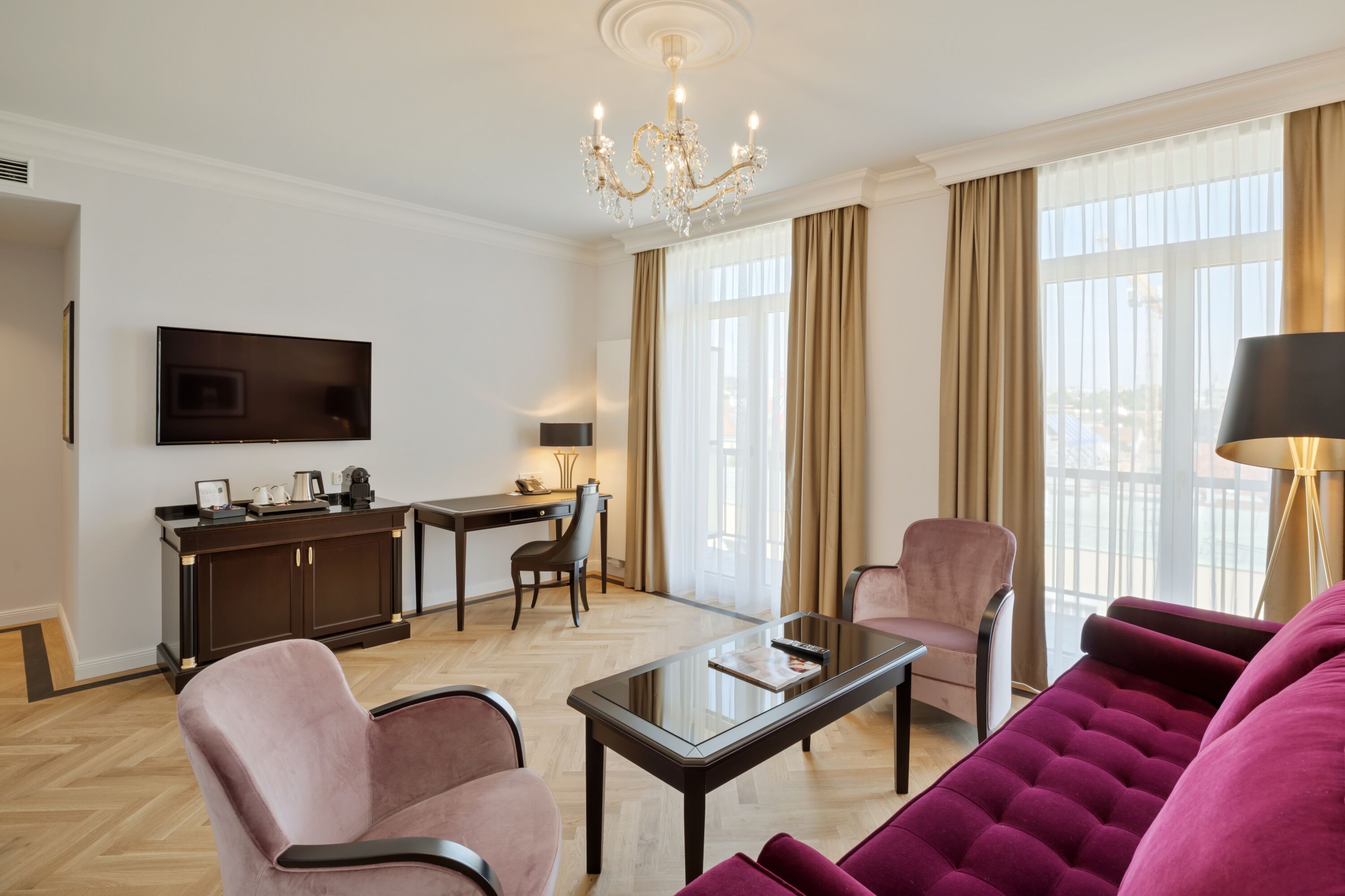 A modern living room with a sofa, armchairs, a coffee table, a TV, and a dining area with a desk and chairs.