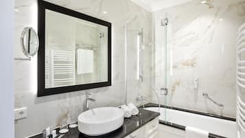 Un baño moderno con un espejo grande, un lavabo blanco, ducha con mampara de vidrio y una bañera.