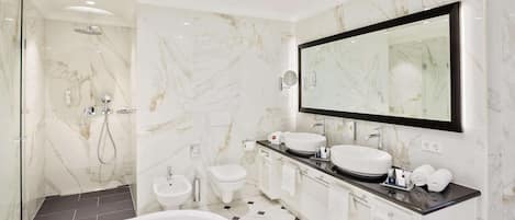 A modern bathroom with a large mirror, two sinks, a bathtub, and a shower area.