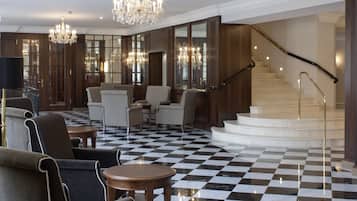 Un vestíbulo amplio con piso a cuadros, elegantes candelabros y una imponente escalera.