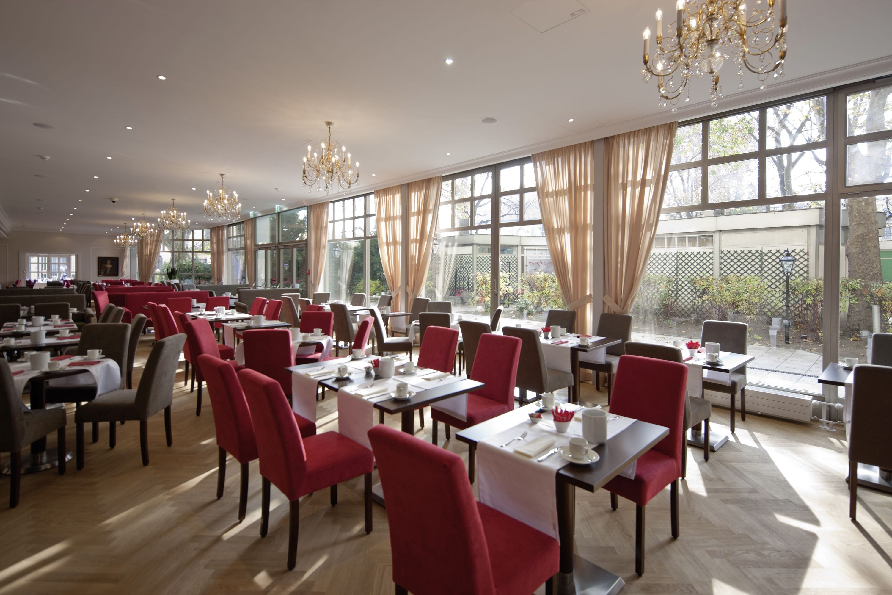 A spacious dining area with red chairs and tables, large windows, and chandeliers.