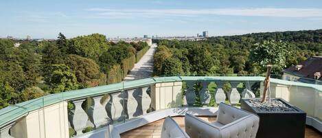 A balcony with a curved glass railing, two white cushioned chairs, and a black rectangular planter.