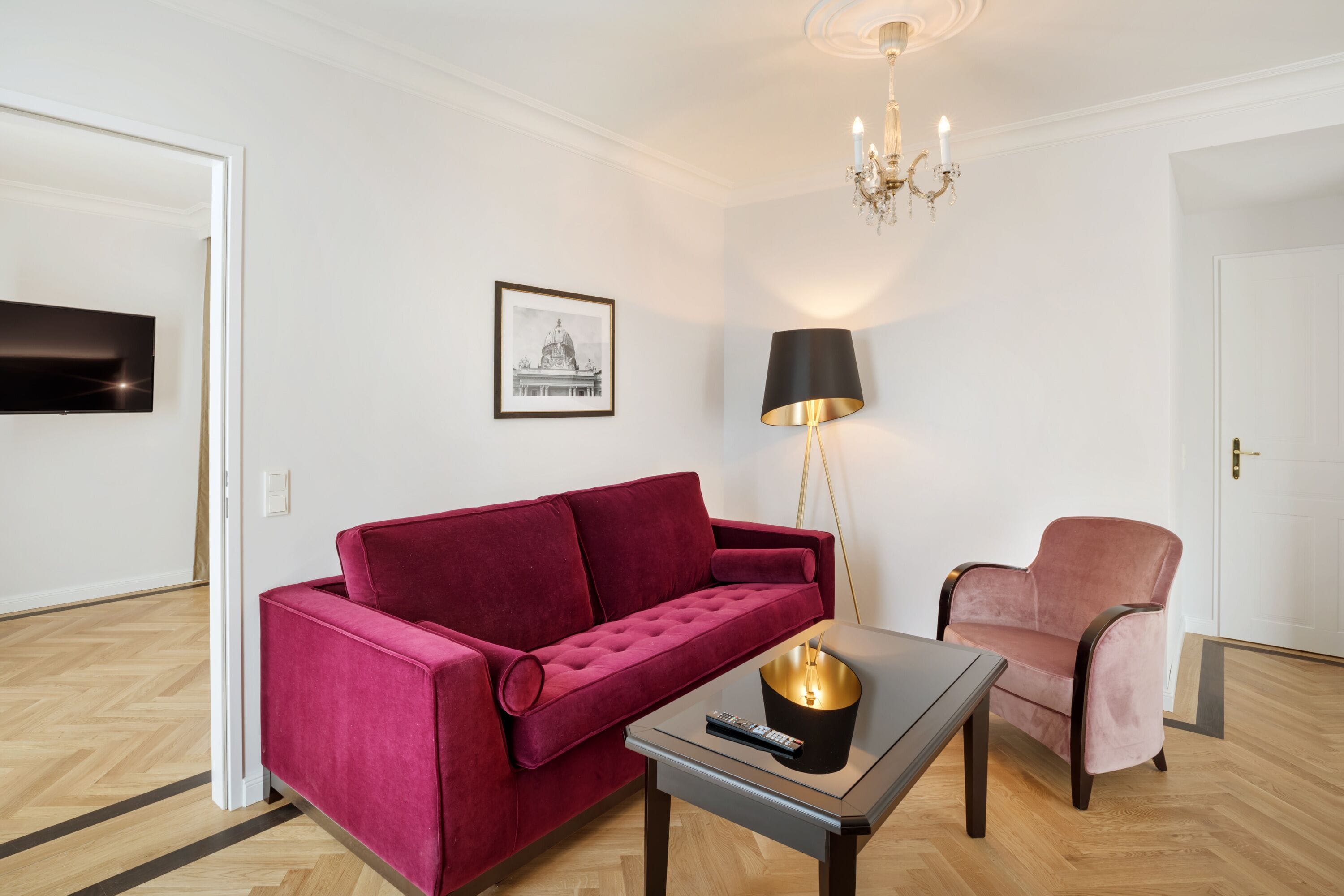A modern living room with a red sofa, a pink armchair, a small table with a lamp, and a framed picture on the wall.