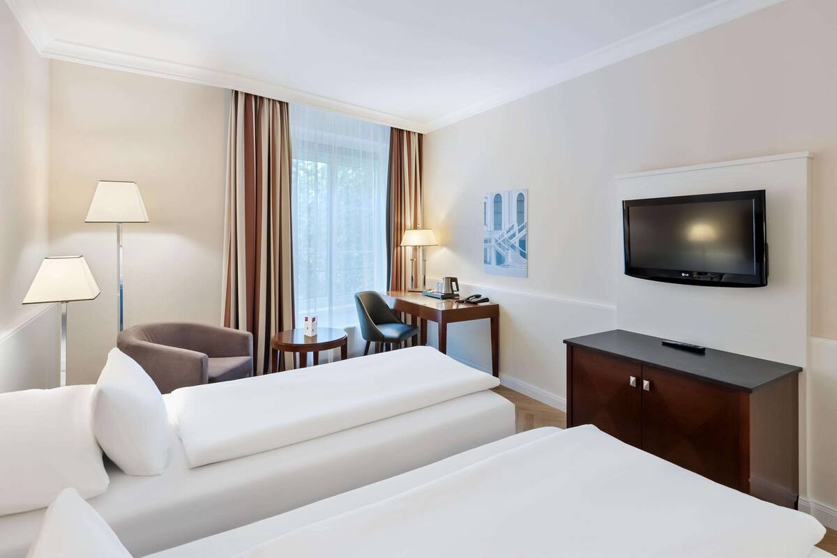 Ein Hotelzimmer mit zwei Betten, einem Schreibtisch, einem Stuhl, einem Fernseher und einer Lampe.