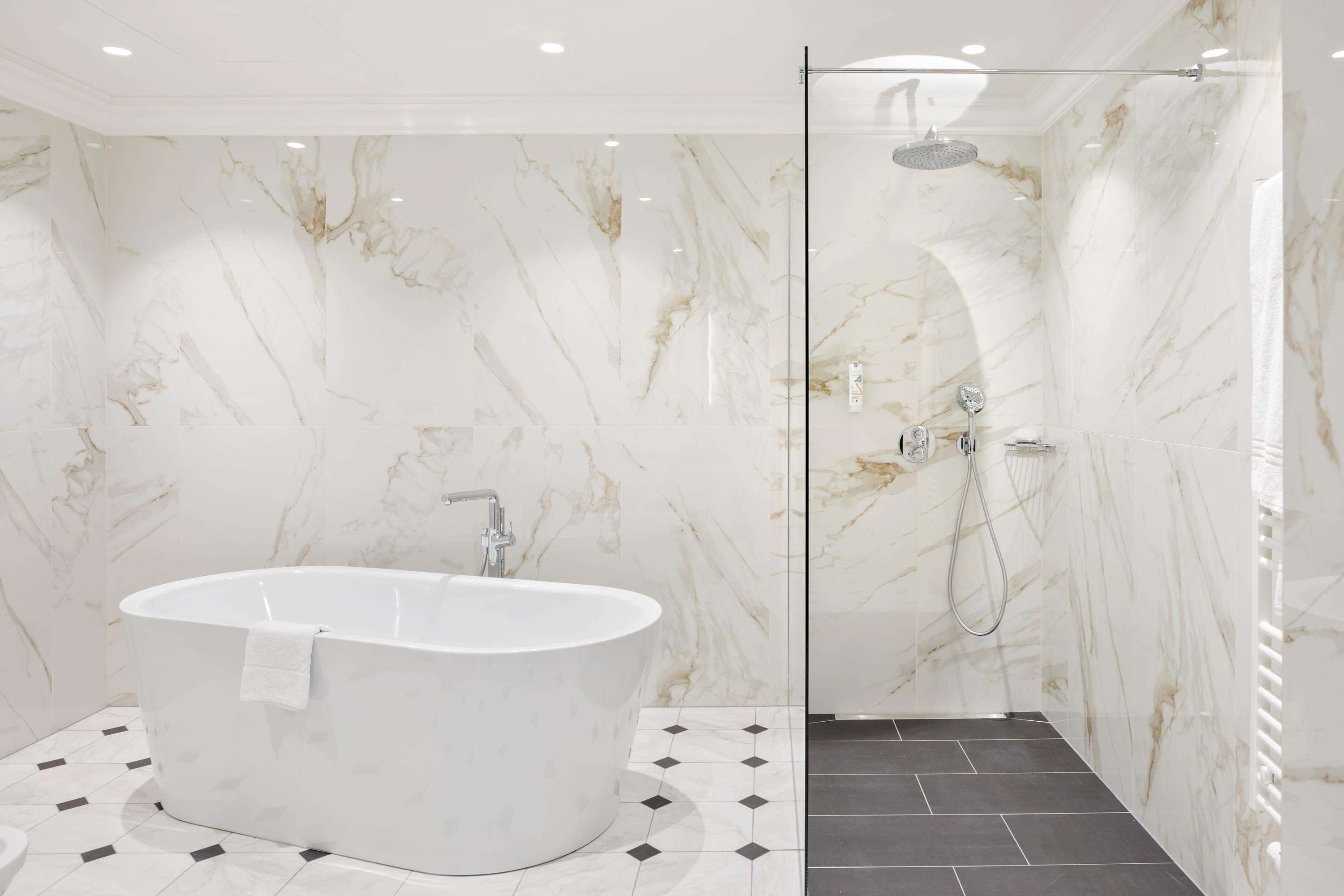 Een moderne badkamer met een vrijstaand bad, een douche met glazen wanden en marmeren muren.