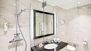Een moderne badkamer met een douche met glazen wand, een grote spiegel, een wastafel en een toilet.