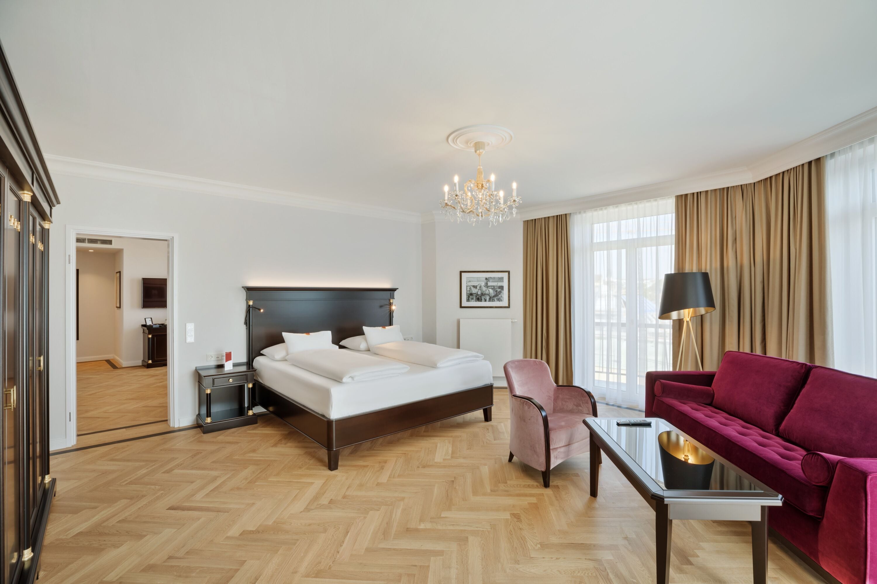 Una habitación de hotel con una cama grande, un escritorio, una silla, un sofá rojo y un candelabro.